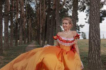 A young woman in an old orange dress walks on the shore of the lake near the castle