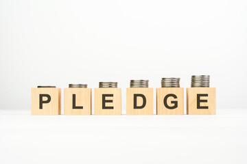 pledge text written on wooden block with stacked coins on white background