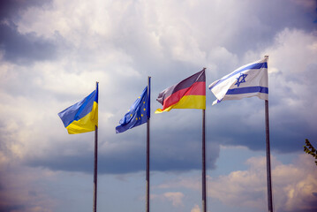 The flag of the European Union and flags of Ukraine, Israel, Germany flutter in the wind in different directions against the blue sky. Bottom side view
