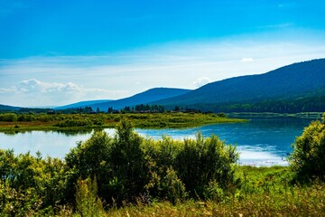 Landscape of the river bank in Siberia. bright juicy colors hilly riverbank and blue clouds