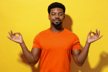 Young spiritual man of African American ethnicity 20s in orange t-shirt hold spreading hands in...