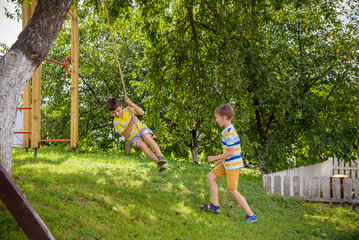 Two adorable happy little boys is having fun on a rope swing which he has found while having rest...