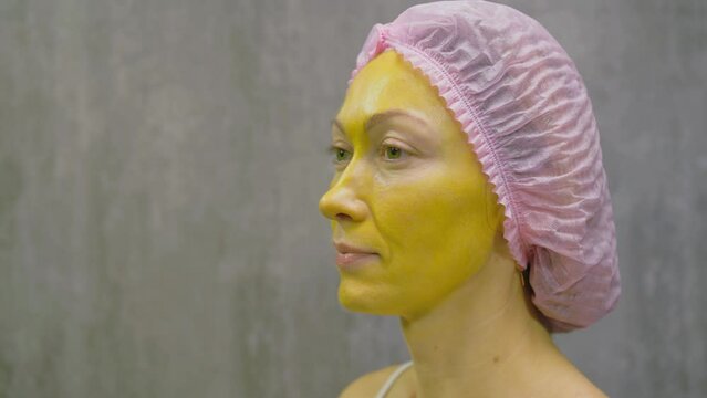 Procedure for skin care to face of young pretty woman. Beauty salon, facial peeling yellow gold alginate mask with retinol treatment, fruit acids. Apply mask on face of model. Cosmetology therapy.