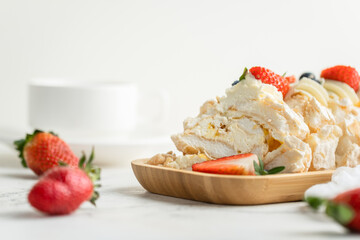 Meringue roll decorated with strawberries and blueberries sliced and served in the wooden plate on the white background. Macro shot