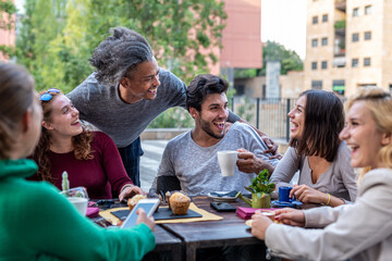 group of multiethnic friends having breakfast with coffee, cappuccino and chocolate muffin, meeting of young people outdoors at a coffee shop