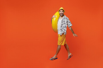 Full body young happy fun tourist man wear beach shirt walking going strolling hold inflatable ring jump isolated on plain orange background studio portrait. Summer vacation sea rest sun tan concept.
