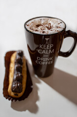 Brown Cup with coffee and dairy foam and inscription "keep calm and drink coffee"on a white background. Chocolate eclair