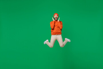 Full body young happy overjoyed excited fun cool caucasian man 20s wear orange sweatshirt hat jump high hold face celebrate isolated on plain green background studio portrait People lifestyle concept