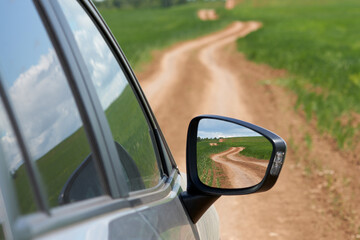 The car is driving along a winding dirt road among a wheat field. The road repeats itself in the...