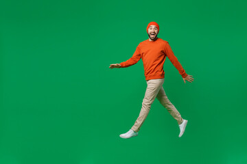 Full body young happy overjoyed excited fun cool man 20s wearing orange sweatshirt hat jump high walking going hurrying celebrate isolated on plain green background studio People lifestyle concept