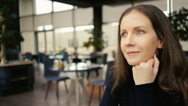 Portrait of woman sitting in restaurant, waiting, thinking, smiling.