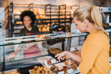 Middle-aged blond woman buying fresh bakery products in bakery.