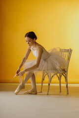 girl tying ballet slippers while sitting on a chair
