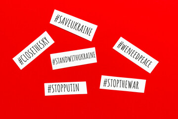 Small paper pieces with words hash tags STOP THE WAR, SAVE UKRAINE, WE NEED PEACE. Flat lay, top view on red background.