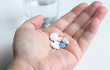 Hand with different kind of pills or drugs and a glass of water