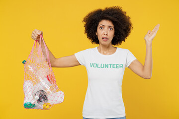 Young woman of African American ethnicity in white volunteer t-shirt hold plastic bag with trash...