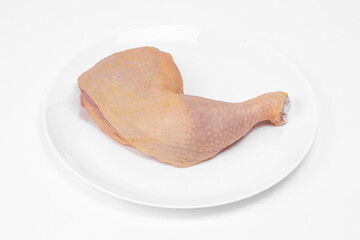 Raw chicken leg quarters on a white ceramic plate, on white background.