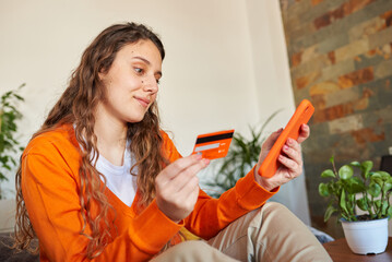 Woman dressed in orange colors shopping with her smartphone from the sofa