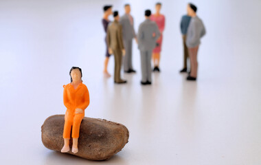 Woman sitting alone excluded from the group of people communicating behind her - symbolised by small figurines