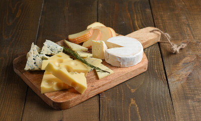 Board with assortment of delicious cheese on board. Wooden background, copy space.
