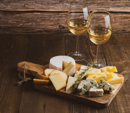 Cheese and a glass of white wine on a wooden background. Different cheeses on a wooden board. Cheese set.