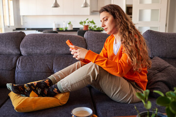Young woman dressed in orange colors using smart phone on sofa