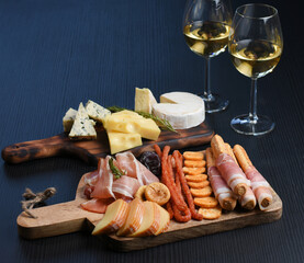 Two white wine glasses with buffet platter with cheese and meats, antipasti, prosciutto, charcuterie.