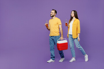 Full body young couple two friends family man woman together wear yellow clothes hold red box freezer cooler refrigerator bottle drink beer walk go isolated on plain violet background studio portrait.