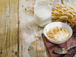 On a wooden table are cereal pads filled with milk, milk in a jug, a spoon and a bouquet of cereals. Whole-grain express breakfasts, family, children's, dietary breakfasts. Vitamins, carbohydrates.