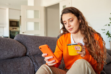 Young woman dressed in orange colors using smart phone on sofa