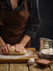 Macro shot. Preparation of dough by the hands of a professional chef on a wooden cutting board, dark background. The concept is the preparation of bread, pizza, pasta, pie, confectionery.