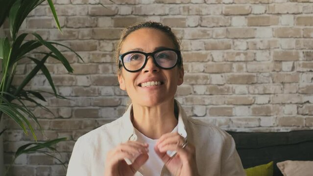Portrait of smiling young woman in eyeglasses looking at camera in front of brick wall. Happy caucasian female tutor giving educational training class lecture or doing video conference call
