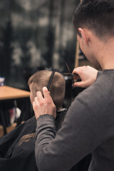 Toddler boy happy to be on the haircut with a professional children's hairdresser. little boy having a haircut at hair salon. Hairdresser's hands making hairstyle to child