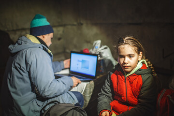 Ukrainian little girl and journalist with notebook sit in a bomb shelter, they wait for the end of...