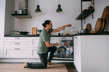 Weekend homework. A young man takes out clean dishes from the dishwasher in the kitchen at home.