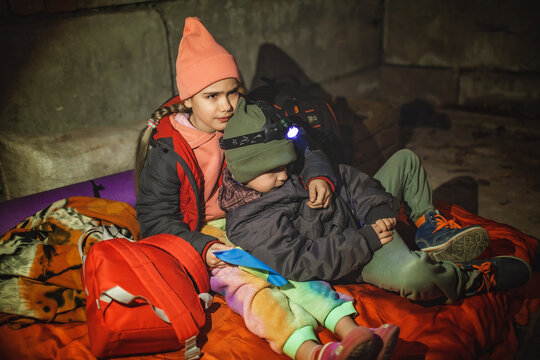 Thoughtful little kids with Ukrainian flag lay in a bomb shelter and waits for the end of the air attack of Russian invaders, terrorism and war, current history