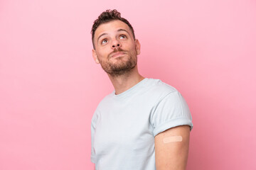 Young Brazilian man wearing a band-aids isolated on pink background looking up while smiling