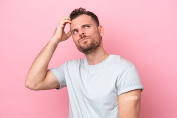 Fototapeta premium Young Brazilian man wearing a band-aids isolated on pink background having doubts and with confuse face expression