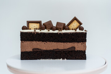 Chocolate cake with cream sponge cake decorated with cookies stands on a white stand on a white background. Isolated background. A tasty treat for a children's birthday party. Pastry craftsmanship.