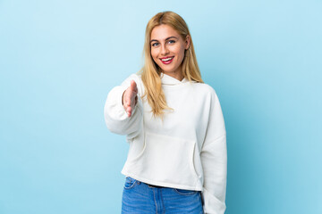 Fototapeta premium Young Uruguayan blonde woman over isolated blue background shaking hands for closing a good deal