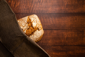 Freshly baked whole wheat bread on wrapped in a gray dishcloth. Dark wooden table background