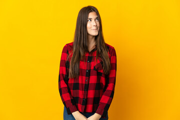 Fototapeta premium Teenager Brazilian girl isolated on yellow background having doubts while looking up