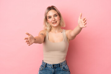 Young caucasian woman isolated on pink background presenting and inviting to come with hand