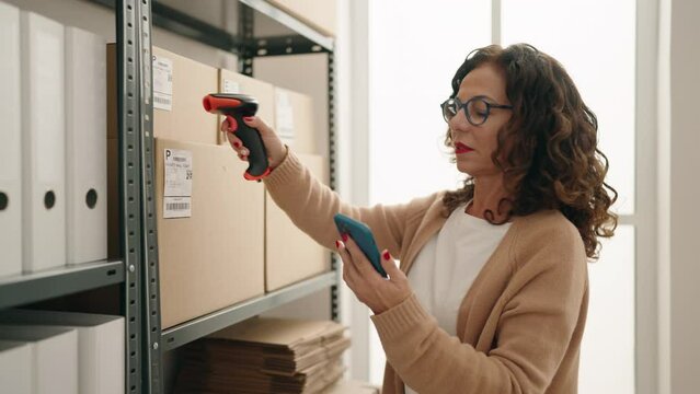 Middle age woman ecommerce business worker scanning package by barcode reader at office