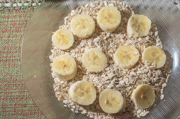 flaked oats and sliced banana, on a plate that is on a table with natural light,copy space in several parts