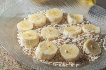 flaked oats and sliced banana, on a plate that is on a table with natural light,copy space in several parts