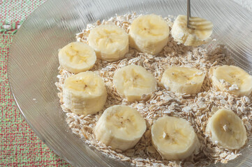 flaked oats and sliced banana, on a plate that is on a table with natural light,copy space in several parts