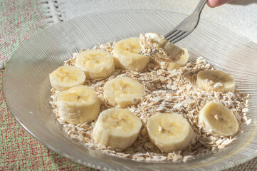 flaked oats and sliced banana, on a plate that is on a table with natural light,copy space in several parts