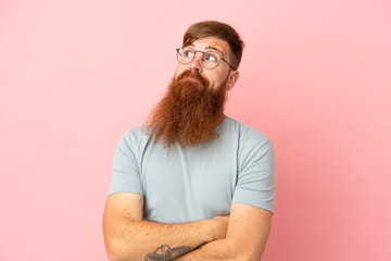 Young reddish caucasian man isolated on pink background making doubts gesture while lifting the...