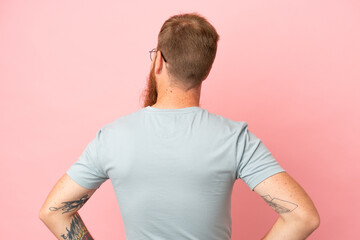 Young reddish caucasian man isolated on pink background in back position and looking side